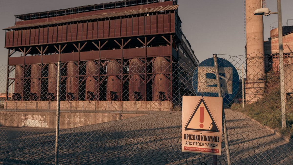 Rusty industrial building with warning sign and fence under warm sunlight.